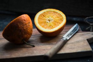 An orange cut in half with a knife beside it.