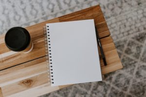 Blank notebook, pen and takeout coffee cup on wooden bench